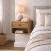 Floating solid mango wood bedside table with curved edges, featuring a drawer and open shelf, styled in a modern bedroom beside a bed with a ceramic lamp and stacked books.