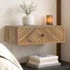 Floating wooden bedside table with chevron-patterned mango wood drawer, styled with a white vase and warm ambient candle.