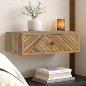 Floating wooden bedside table with chevron-patterned mango wood drawer, styled with a white vase and warm ambient candle.
