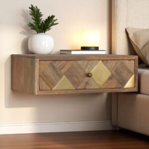 Floating wooden bedside table with brass inlay drawer, styled with a white vase, greenery, books, and a small glowing lamp beside a bed.