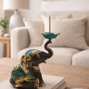 Decorative elephant incense holder with a raised trunk, finished in antique gold and green detailing, styled on a wooden surface in a warm, softly lit living space with neutral décor.