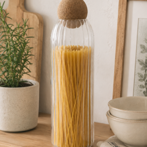 Tall ribbed glass storage jar with cork ball lid, filled with spaghetti, styled on a wooden kitchen shelf with neutral décor and soft natural light.