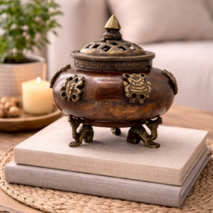 Antique style incense burner with decorative brass lid and elephant feet, displayed on stacked books on a wooden table in a warm, cosy living room setting.