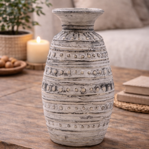 Textured cream ceramic decorative vase with carved pattern, styled on a wooden table with books and greenery in a warm, neutral living room setting.