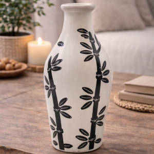 Cream ceramic decorative vase with black bamboo pattern, styled on a wooden console table with books and greenery in a calm, neutral living room setting.