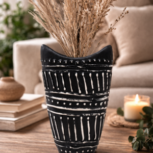 Black ceramic decorative vase with white tribal pattern, styled on a wooden coffee table with books, a candle and greenery in a warm, cosy living room setting.