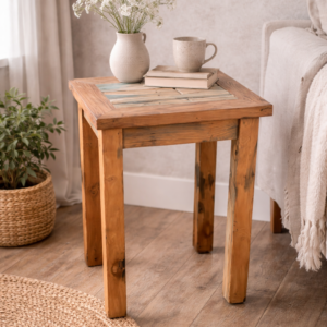 Rustic reclaimed wood side table with mosaic-style wooden top, styled beside a sofa with a ceramic vase of flowers and books in a warm, natural living room setting.