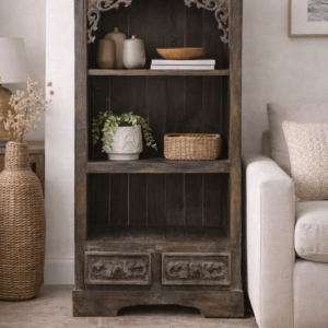Hand-carved dark wood cabinet with open shelving and two drawers, styled in a neutral living room with soft furnishings, woven textures, decorative ceramics, and natural light.