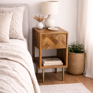 Solid mango wood bedside table with herringbone drawer front and open shelf, styled in a neutral bedroom with soft bedding, lamp, and woven plant pot.