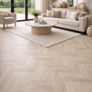 Light oak herringbone engineered wood flooring with a subtle grey-washed beige tone, shown in a bright modern living room with neutral furnishings, emphasising the floor’s natural grain and pattern as the main feature.
